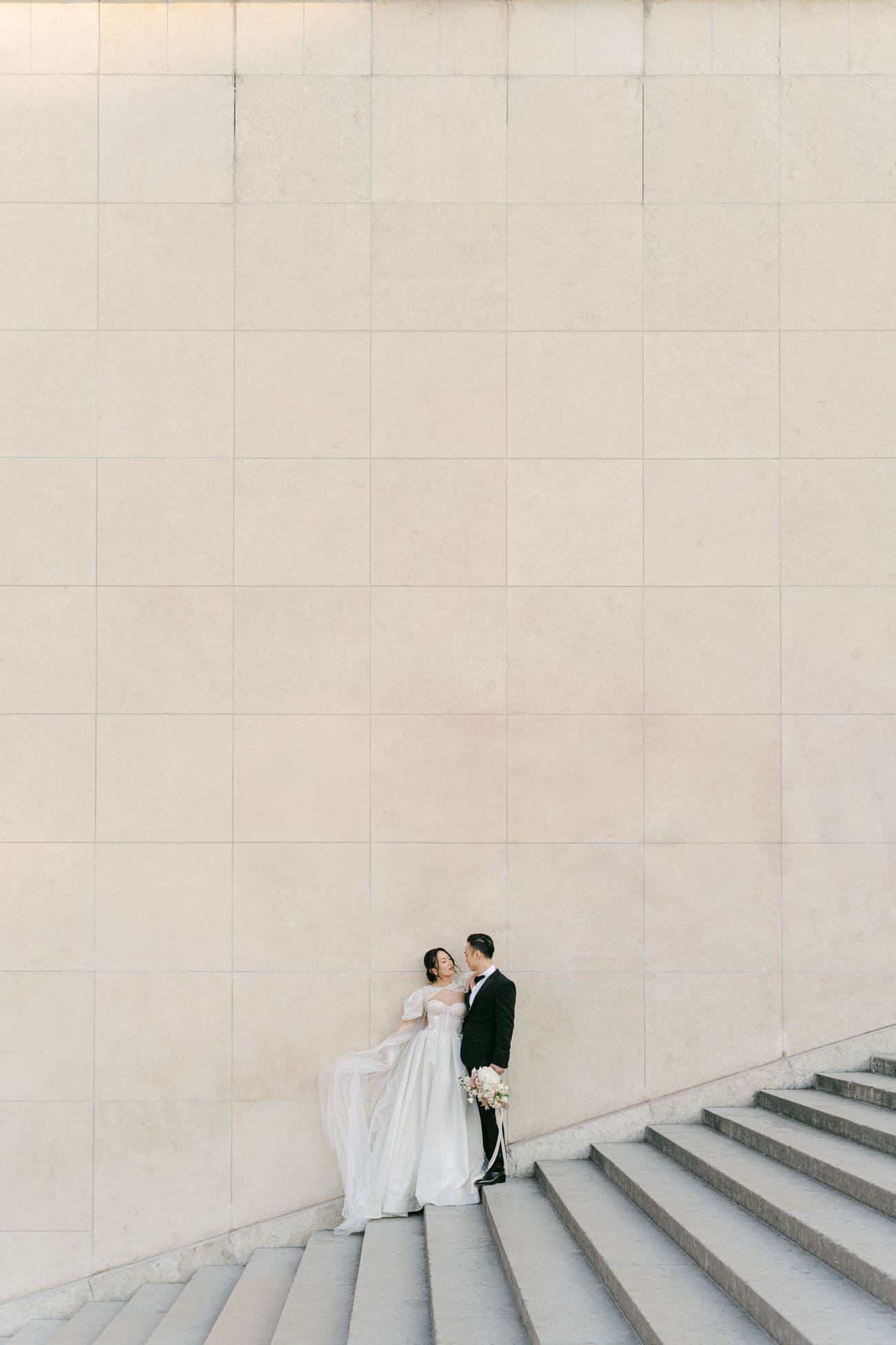Ein Brautpaar teilt einen intimen Moment auf einer Treppe, eingebettet in die großflächige, nüchterne Architektur, die eine einzigartige Kulisse für ihre Hochzeitsfotos bietet.